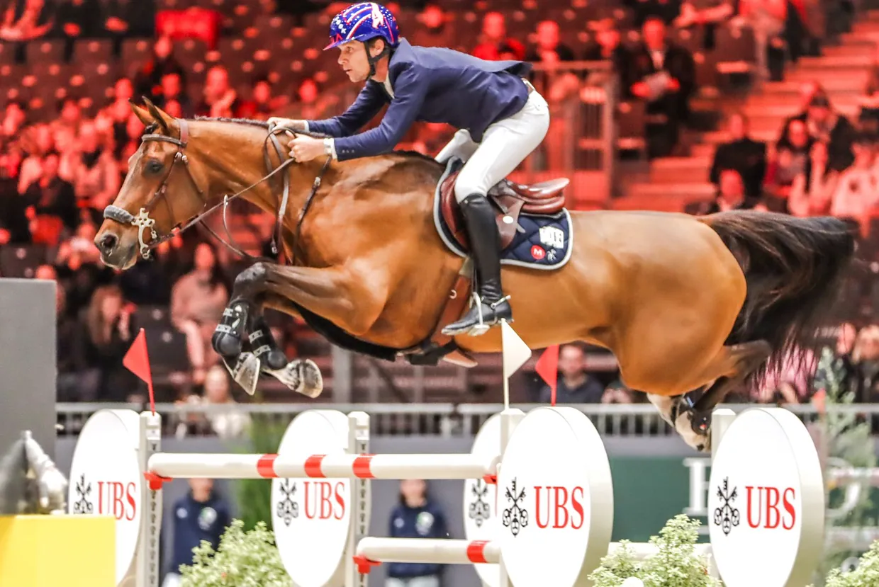 Show jumping horse and rider clearing a fence at an international indoor competition
